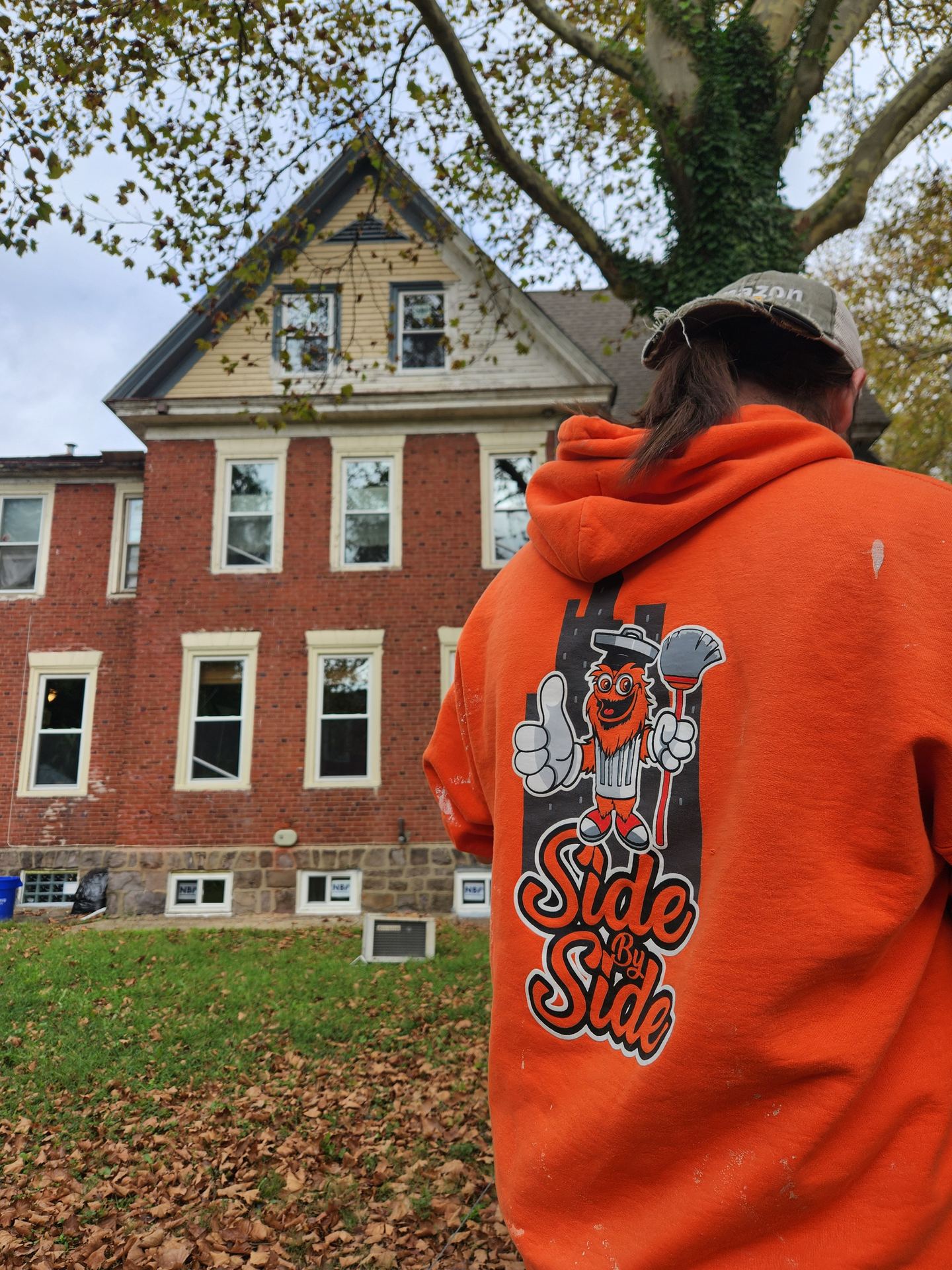 Side by Side crew member in an orange Side by Side hoodie outside a brick home