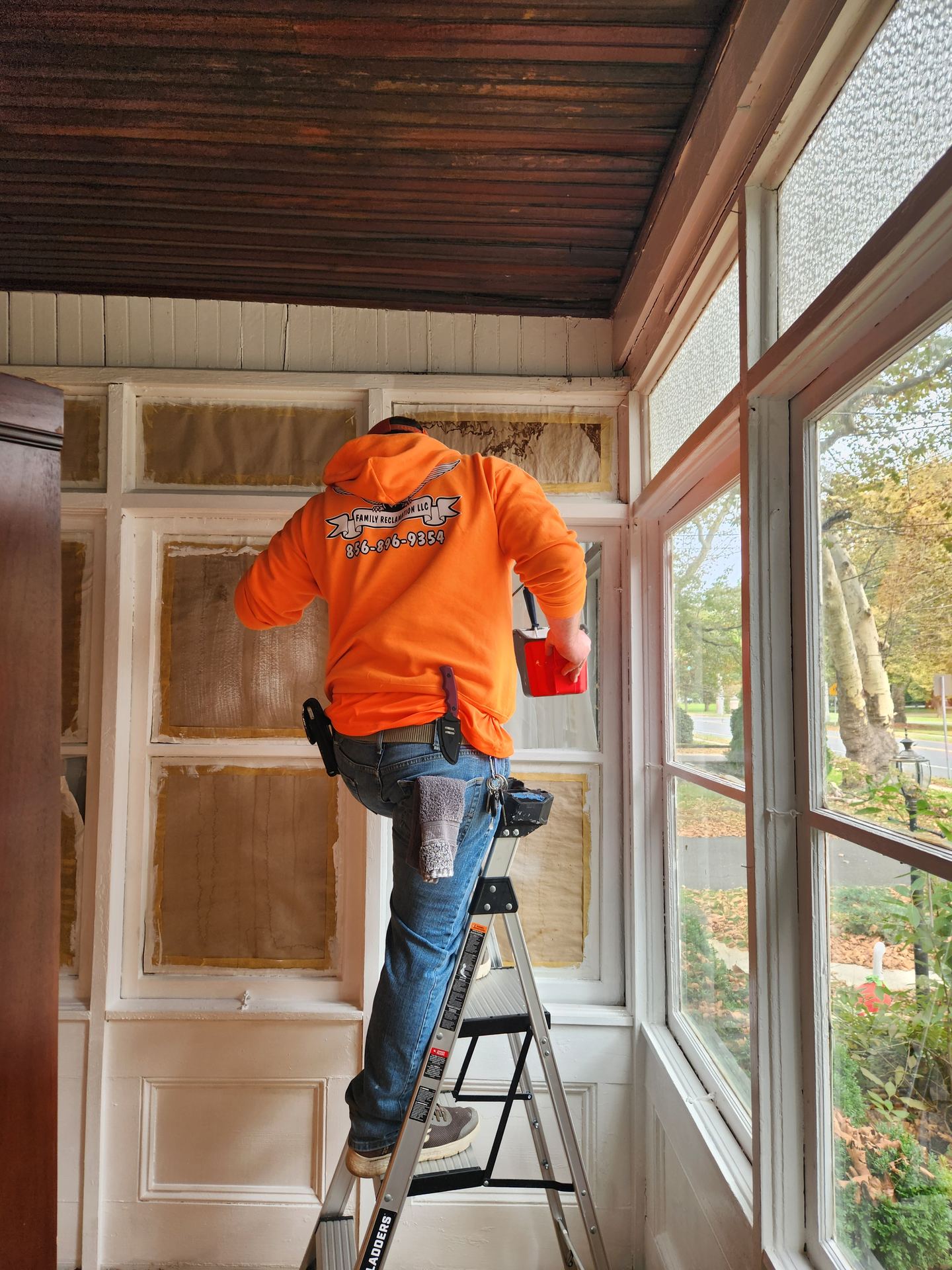 Side by Side technician on a ladder working on a sunroom window frame